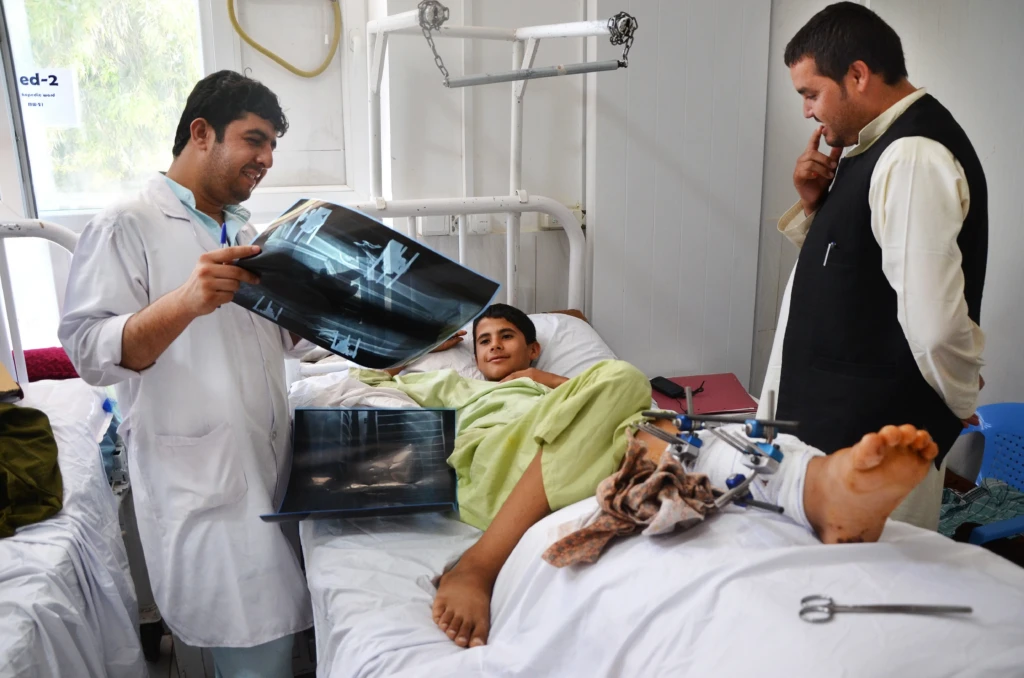 El fisioterapeuta de MSF, Baryali Baloch (izquierda), examina las radiografías, el 28 de mayo de 2016, de un niño de 14 años de la provincia de Helmand, que se recupera de una operación por fracturas en el hospital Boost de Lashka Ghar, provincia de Helmand, Afganistán. © Kate Stegeman/MSF