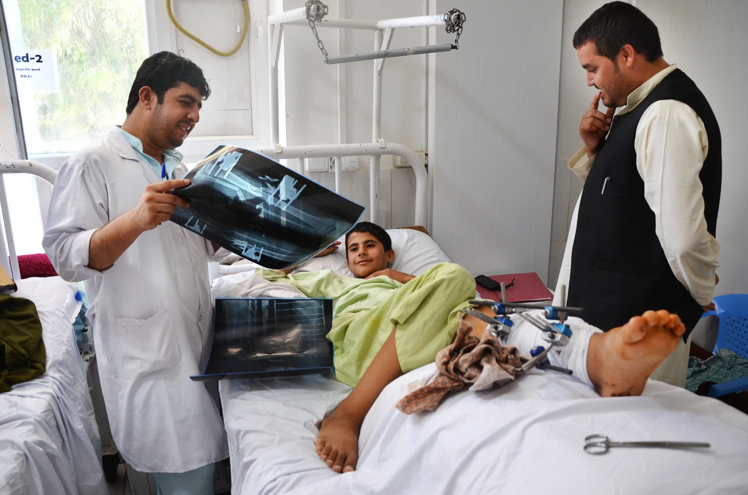 El fisioterapeuta de MSF, Baryali Baloch (izquierda), examina las radiografías, el 28 de mayo de 2016, de un niño de 14 años de la provincia de Helmand, que se recupera de una operación por fracturas en el hospital Boost de Lashka Ghar, provincia de Helmand, Afganistán. © Kate Stegeman/MSF