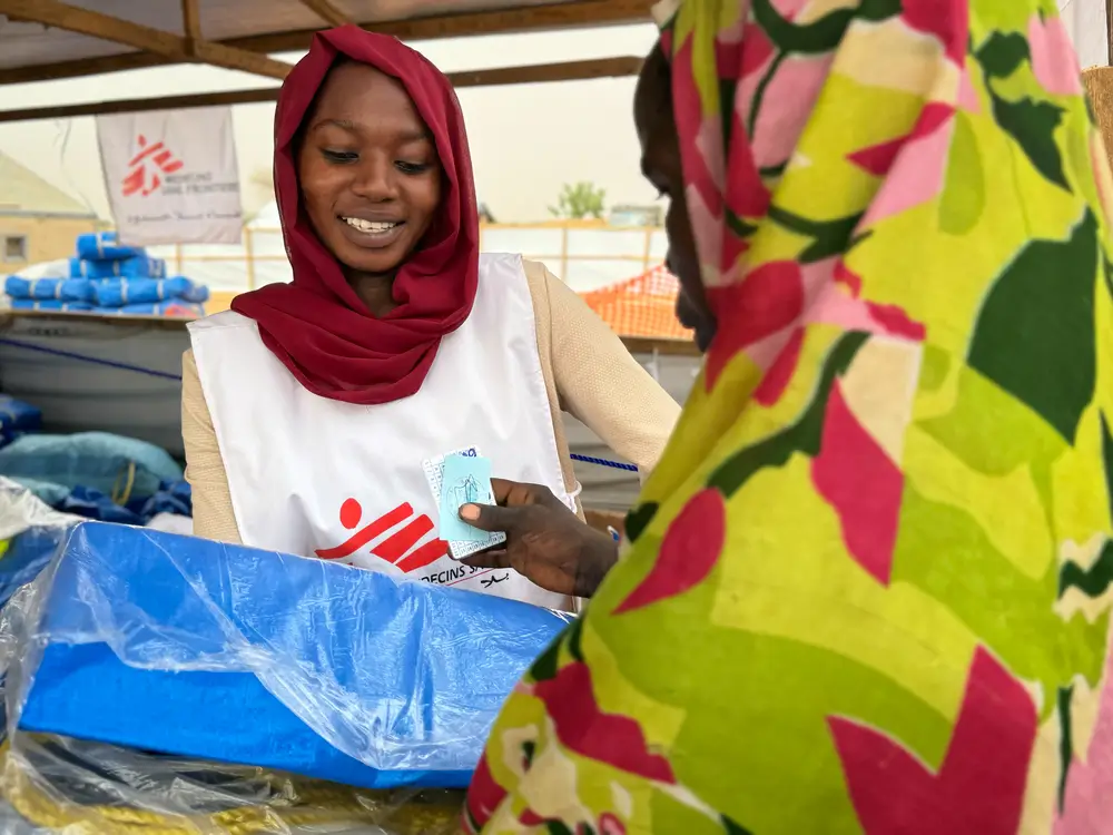 Personal de Médicos SIn Fronteras entrega un kit con una lona plástica, cuerdas y pastillas de jabón a una mujerrefugiada en el campo de Adré