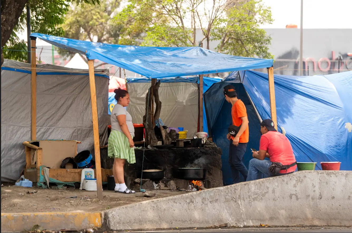 Personas migrantes fuera de su tienda en un campamento informal en Ciudad de México (CDMX).