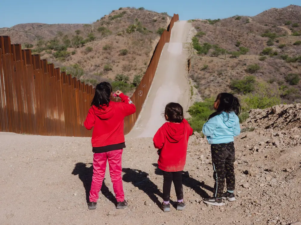 Tres niñas migrantes jugando con burbujas en la frontera de México y Estados Unidos.