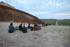 Migrantes y solicitantes de asilo de Bangladesh y Nepal esperan a que la Patrulla Fronteriza de Estados Unidos los recoja en la carretera sin pavimentar junto al muro fronterizo entre Estados Unidos y México en Sasabe, Arizona.