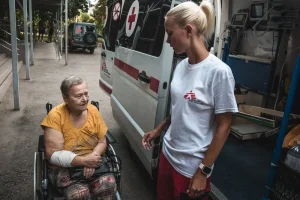 Diana Bilonozhko ayuda a una paciente a sentarse en la ambulancia después de un procedimiento de diálisis.