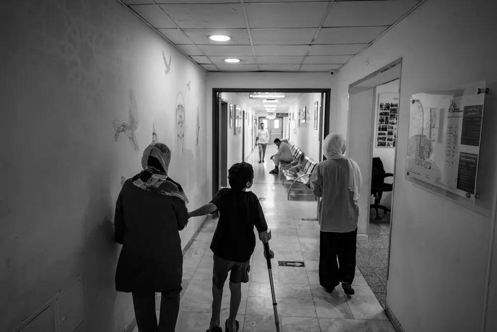 Hazem (centro), camina junto a su madre Eman (izquierda) y su hermana Deema (derecha) en el pasillo del hospital de cirugía reconstructiva de MSF en Ammán.