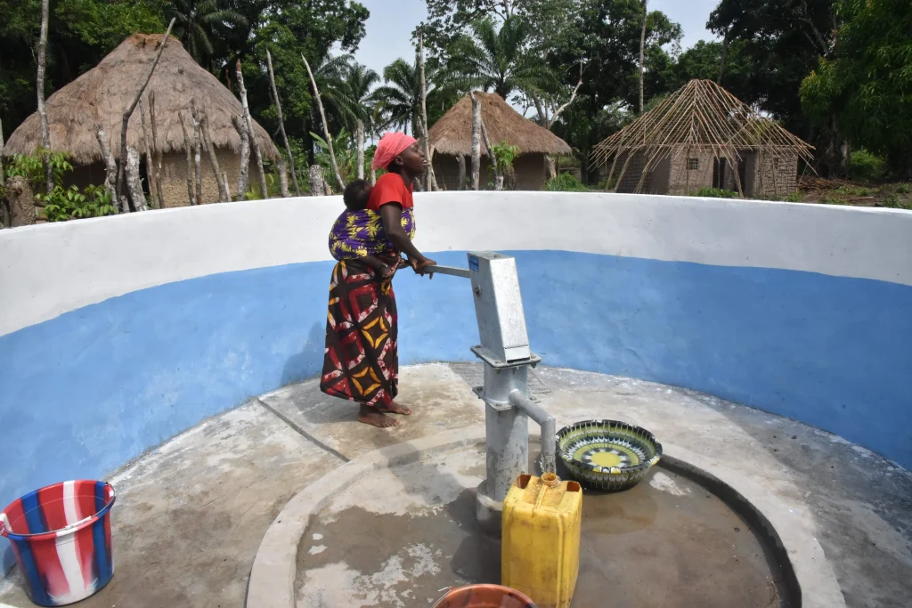 Aminata Bangura utiliza una bomba manual para sacar agua de un pozo perforado por MSF, con su hijo atado a la espalda, en la aldea de Masiperr, distrito de Tonkolili, Sierra Leona. © Daniel García / MSF