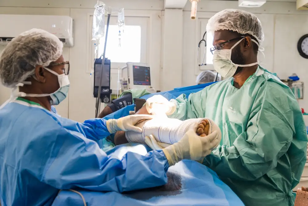 Un paciente herido de bala en el pie durante los enfrentamientos entre grupos armados y las fuerzas de policía recibe atención en el quirófano del hospital MSF de Tabarre. Haití 2024.