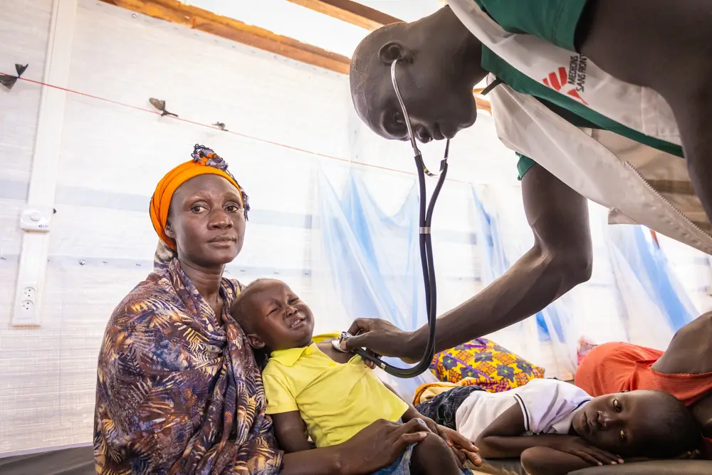 Un enfermero de MSF examina a Atak Daniel, de 2 años, con un estetoscopio mientras su madre lo tranquiliza. Nueva sala de malaria del Hospital Estatal de Aweil.