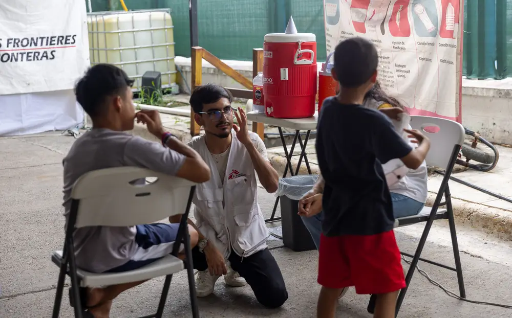 Trabajador de MSF conversa con dos niños en el albergue Pumarejo, en Matamoros, México, donde brindamos atención a personas migrantes.