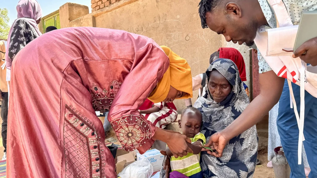 Un voluntario comunitario y un miembro del personal de MSF realizan un cribado MUAC, en Mohamed Ayoub, de 18 meses, inmediatamente después de su vacunación contra el sarampión. El Geneina, Sudán.