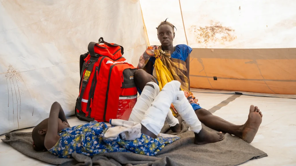 Nyachan Chan se sienta junto a su hija de nueve años, que tiene graves quemaduras en ambas extremidades inferiores, mientras esperan la derivación a la clínica Chuil en el estado de Jonglei, Sudán del Sur.