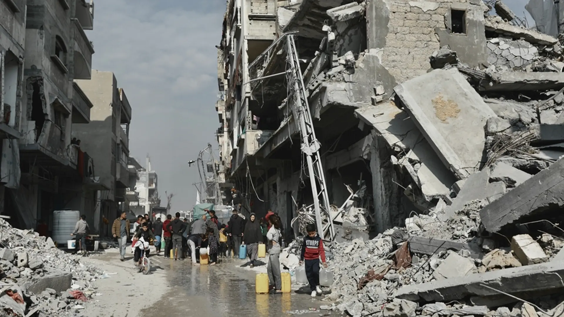 La gente recoge agua junto a un edificio que está en peligro de derrumbarse en Beit Lahia, Gaza.