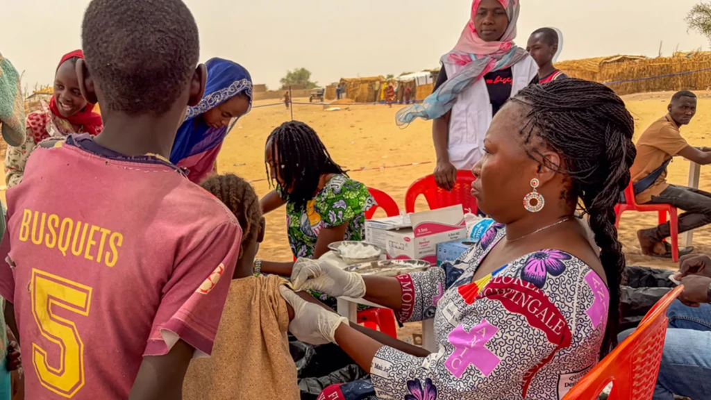 Mujeres y niños se reúnen en un punto de vacunación en un asentamiento de refugiados en Adré, donde el hacinamiento y la inmunización rutinaria limitada aumentan el riesgo de transmisión del sarampión.
