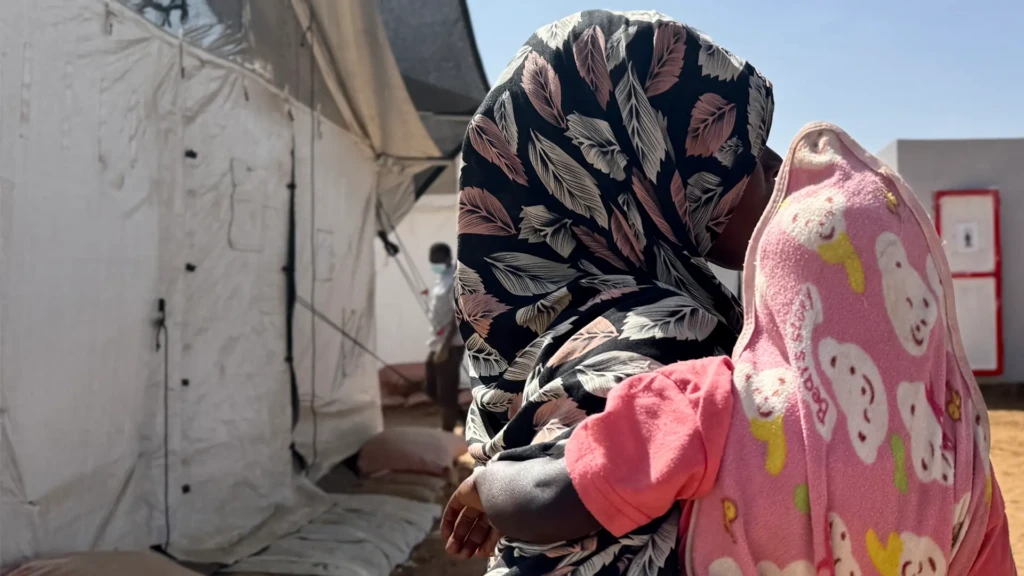 Amina* abraza a un niño frente a un refugio improvisado en Tawila. Mientras huía de El Fasher con sus hijos, fue violada por hombres armados. Darfur Norte, Sudán, febrero de 2026.