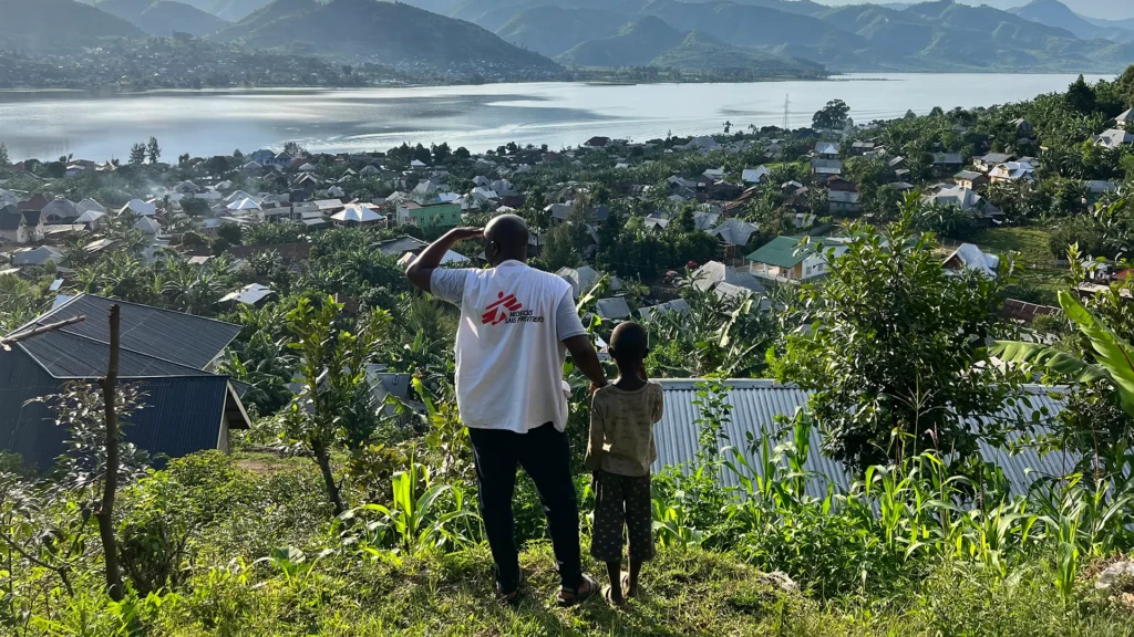 Un miembro de MSF y un niño contemplan la ciudad de Minova y el lago Kivu desde lo alto de una colina en la provincia de Kivu del Sur, República Democrática del Congo.