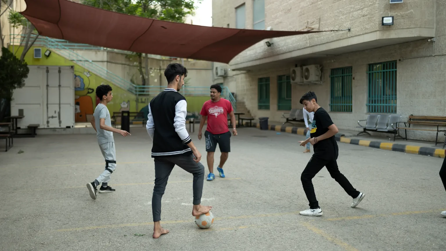 Ali, Mohamed H. y varios otros pacientes del hospital MSF en Ammán juegan al fútbol en el patio del hospital. Como deporte popular entre muchas nacionalidades de la región, el departamento de salud mental del hospital organiza partidos semanales de fútbol entre los pacientes. Hospital MSF, Ammán, Jordania. Abril de 2024.