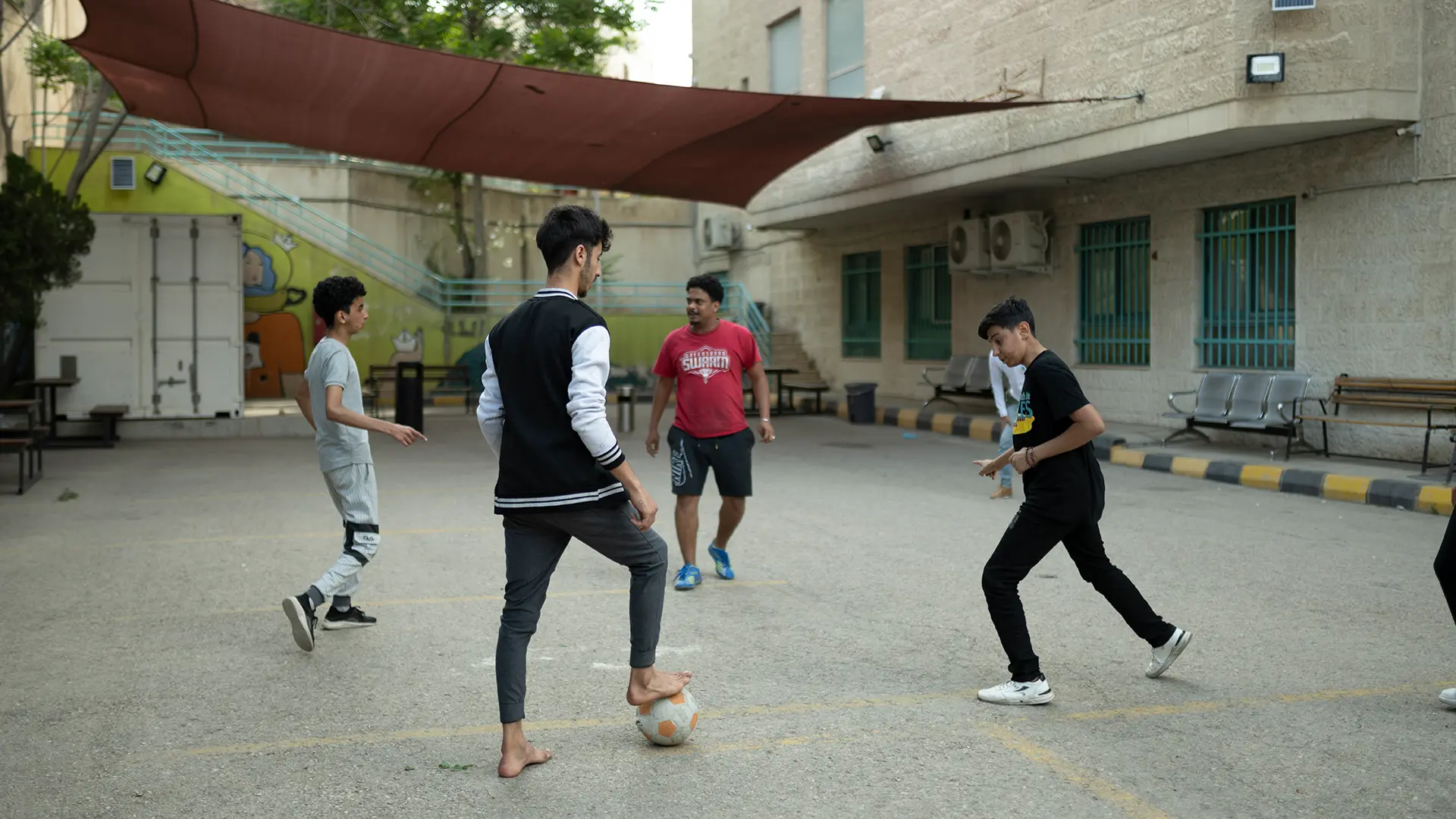 Ali, Mohamed H. y varios otros pacientes del hospital MSF en Ammán juegan al fútbol en el patio del hospital. Como deporte popular entre muchas nacionalidades de la región, el departamento de salud mental del hospital organiza partidos semanales de fútbol entre los pacientes. Hospital MSF, Ammán, Jordania. Abril de 2024.