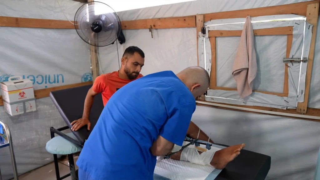 Un personal de MSF revisa la lesión de Saad Hussein, que se ve obligado a vivir con un fijador externo tras resultar herido en 2025 durante una distribución de alimentos por parte de la Fundación Humanitaria de Gaza. Centro de atención primaria Al Mawasi, Khan Younis, Gaza.