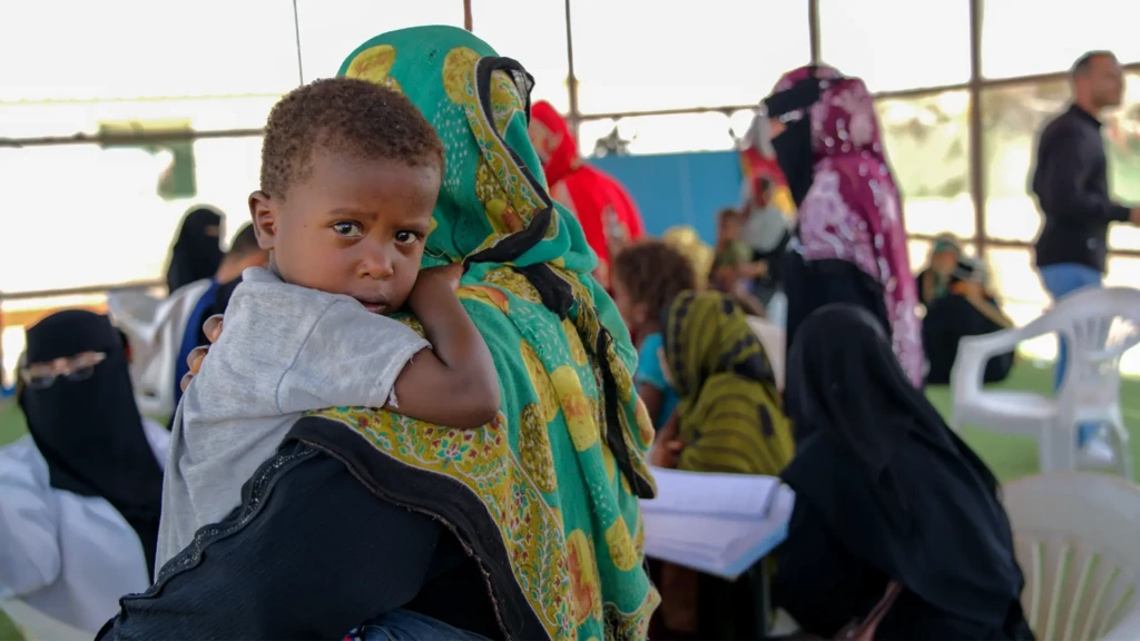 Eftikhar Ahmed sostiene a su hijo de tres años, Badr, mientras las familias esperan durante una campaña de vacunación contra el sarampión en un campo para desplazados en el campo de Ateera (2), distrito de Tuban, gobernación de Lahj, Yemen, 5 de mayo de 2026.