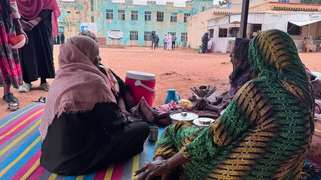 Mujeres se sientan alrededor de ollas de comida en uno de los mayores campos de refugiados de El Obeid, Sudán, en julio de 2026.