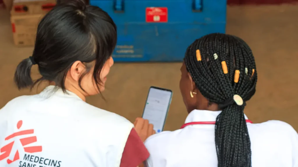 La Dra. Anaïs Kale-Mea-Kale y Dra. Kana Yamada revisan los resultados médicos utilizando la aplicación móvil del servicio de gestión de casos de telemedicina en la entrada de la sala pediátrica del Hospital Carnot, RCA.