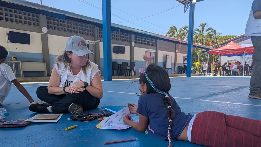 Carolina López, responsable de actividades de salud mental de MSF, guía a un niño en una sesión de psicoeducación durante una actividad móvil de salud mental en Naiguatá, La Guaira.