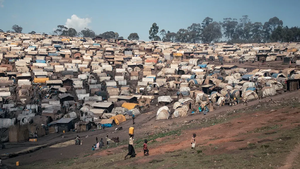 Unos niños transportan recipientes de agua por el campo de Plaine Savo, cerca de Fataki, donde residen aproximadamente 76,000 personas desplazadas. RDC.