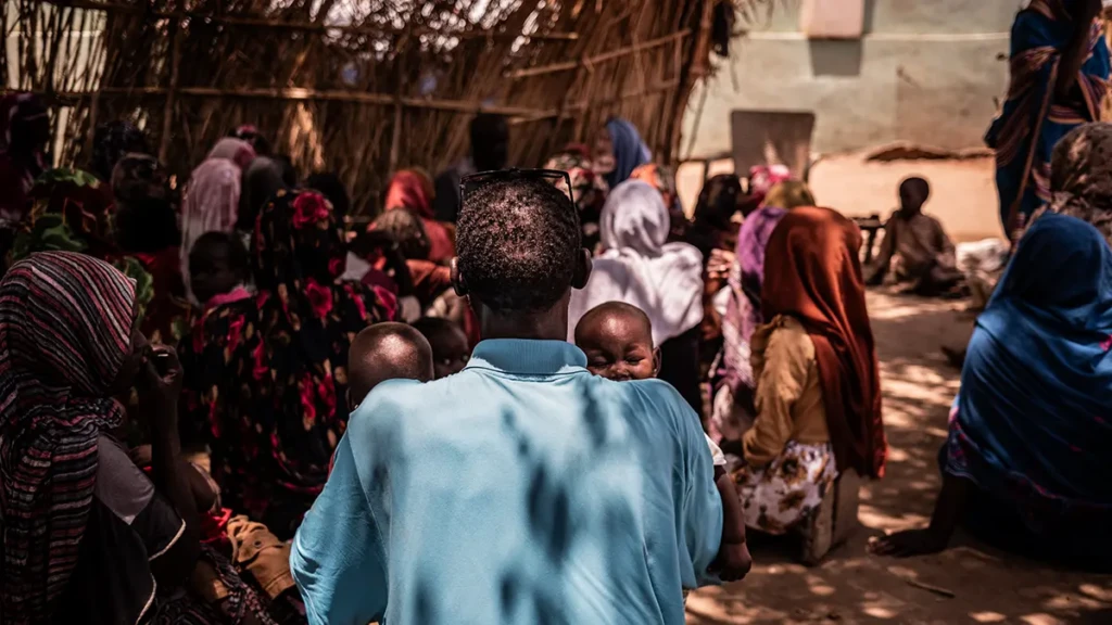 Mohammed Khamis sostiene a sus dos hijos durante una conversación con el equipo de participación comunitaria de MSF en la escuela convertida en campo de desplazados internos donde viven.