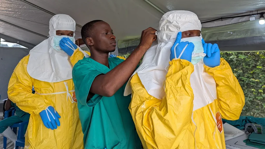 El personal del Centro de Tratamiento del Ébola del Hôpital du Cinquantenaire, en Kisangani, ayuda a sus compañeros a colocarse el equipo de protección individual (EPI) antes de entrar en la zona de alto riesgo.