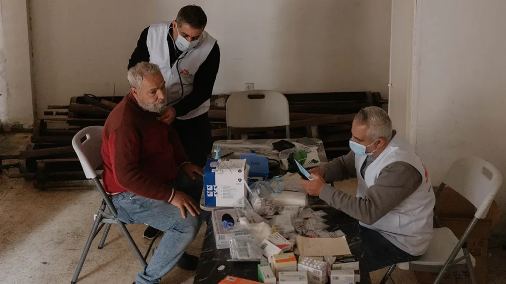 Un médico escucha a través de un estetoscopio los sonidos torácicos de un hombre desplazado mientras una enfermera de MSF registra sus signos vitales.