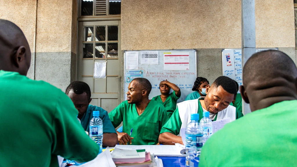 Todo el equipo multidisciplinario, compuesto por médicos y personal de enfermería de los turnos de día y de noche, realiza el traspaso de actividades en el despacho médico del Centro de Tratamiento del Ébola del Hospital General de Kitatumba. © Lucie Ringué/MSF