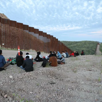 Migrantes y solicitantes de asilo de Bangladesh y Nepal esperan a que la Patrulla Fronteriza de Estados Unidos los recoja en la carretera sin pavimentar junto al muro fronterizo entre Estados Unidos y México en Sasabe, Arizona.