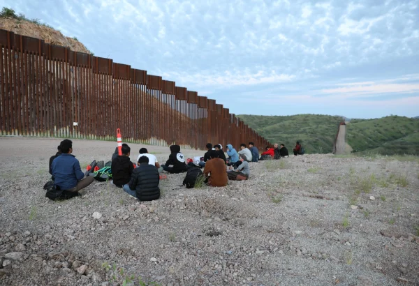 Migrantes y solicitantes de asilo de Bangladesh y Nepal esperan a que la Patrulla Fronteriza de Estados Unidos los recoja en la carretera sin pavimentar junto al muro fronterizo entre Estados Unidos y México en Sasabe, Arizona.