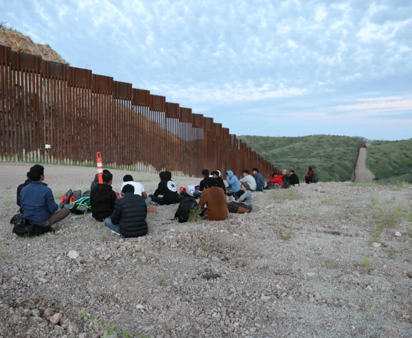 Migrantes y solicitantes de asilo de Bangladesh y Nepal esperan a que la Patrulla Fronteriza de Estados Unidos los recoja en la carretera sin pavimentar junto al muro fronterizo entre Estados Unidos y México en Sasabe, Arizona.