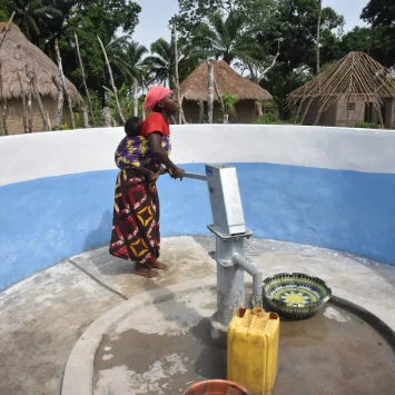 Aminata Bangura utiliza una bomba manual para sacar agua de un pozo perforado por MSF, con su hijo atado a la espalda, en la aldea de Masiperr, distrito de Tonkolili, Sierra Leona. © Daniel García / MSF