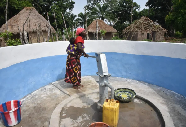 Aminata Bangura utiliza una bomba manual para sacar agua de un pozo perforado por MSF, con su hijo atado a la espalda, en la aldea de Masiperr, distrito de Tonkolili, Sierra Leona. © Daniel García / MSF