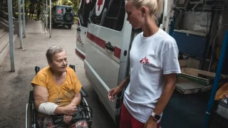 Diana Bilonozhko ayuda a una paciente a sentarse en la ambulancia después de un procedimiento de diálisis.