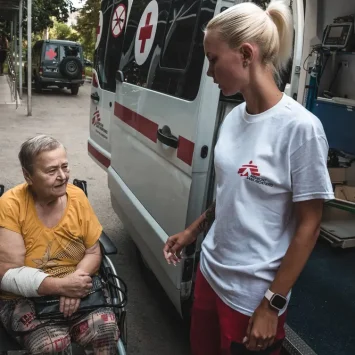 Diana Bilonozhko ayuda a una paciente a sentarse en la ambulancia después de un procedimiento de diálisis.