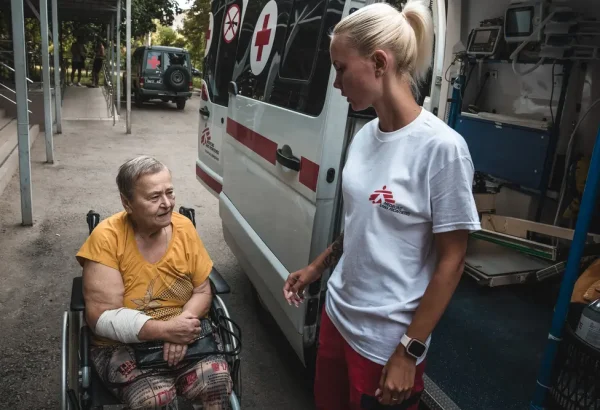 Diana Bilonozhko ayuda a una paciente a sentarse en la ambulancia después de un procedimiento de diálisis.